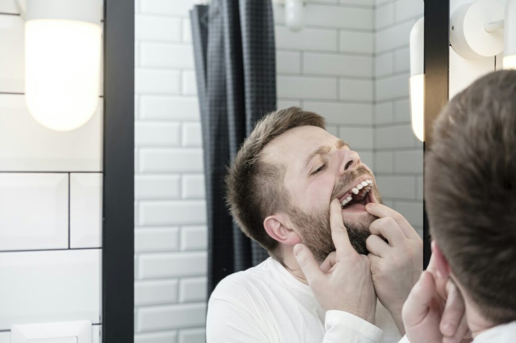 Man examining missing tooth in mirror, needs emergency dental care at Brentwood Family Dentistry.