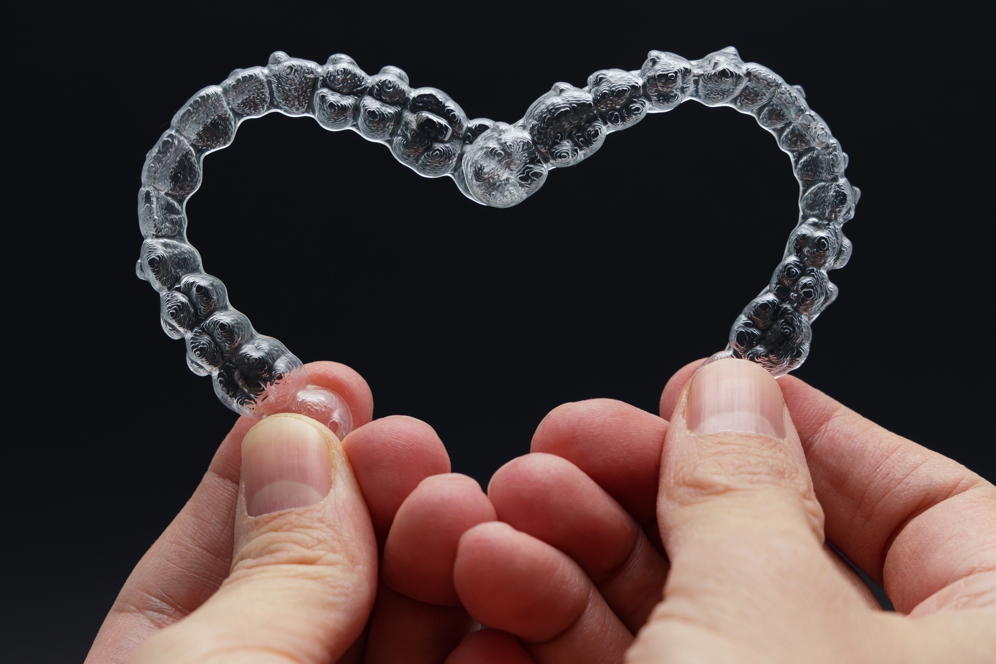 Hands holding Invisalign clear aligners shaped like a heart, representing comfortable, discreet teeth straightening at Brentwood Family Dentistry in Brentwood, MO